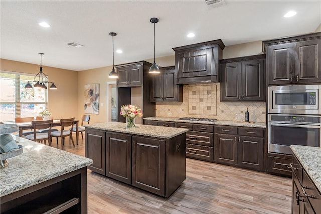 kitchen with appliances with stainless steel finishes, light wood-type flooring, custom range hood, and tasteful backsplash