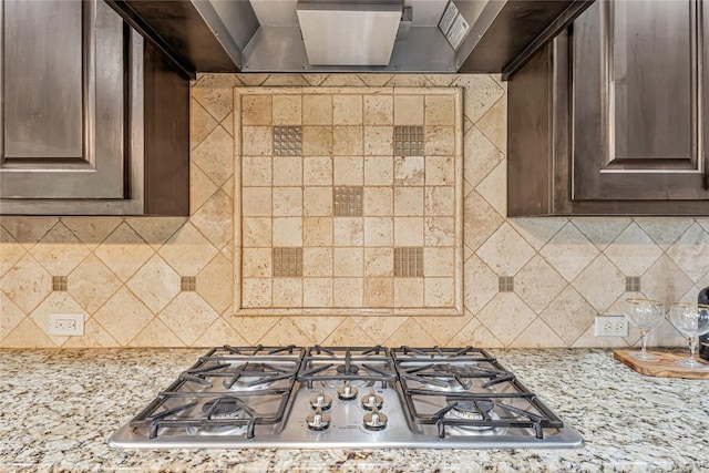 kitchen with stainless steel gas cooktop, light stone counters, backsplash, and dark brown cabinetry