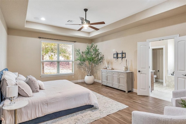 bedroom with a tray ceiling, light wood-type flooring, visible vents, and baseboards