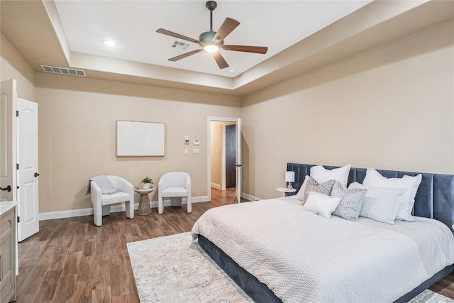 bedroom featuring a tray ceiling, baseboards, visible vents, and wood finished floors