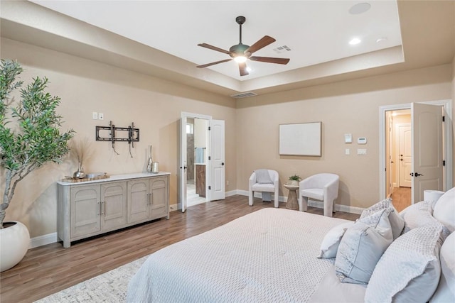 bedroom with a raised ceiling, visible vents, baseboards, and light wood finished floors