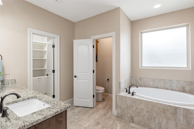 full bath featuring baseboards, toilet, a garden tub, a walk in closet, and vanity