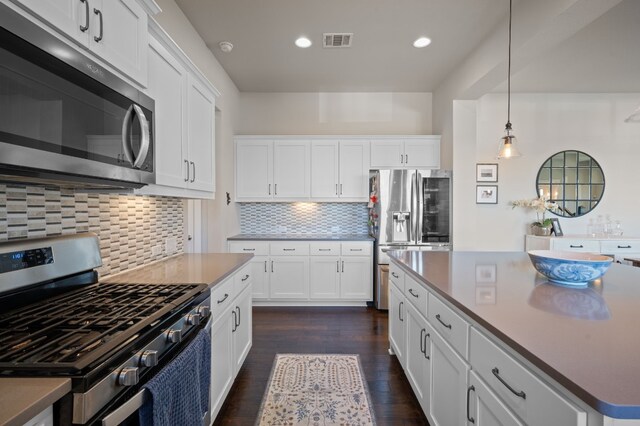 kitchen featuring white cabinets, backsplash, appliances with stainless steel finishes, dark hardwood / wood-style floors, and pendant lighting