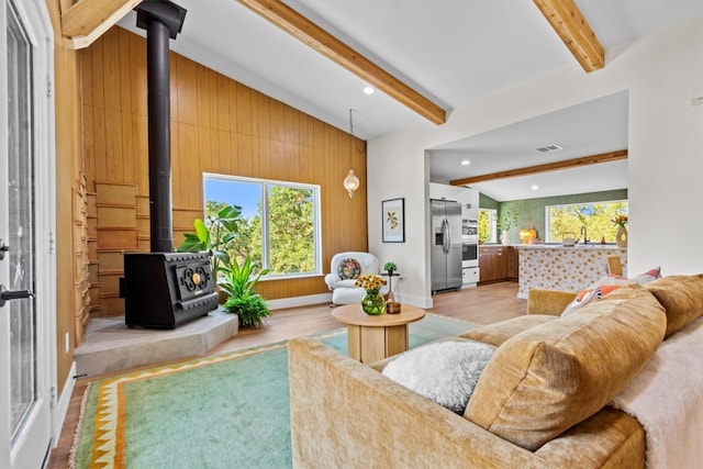 living room with lofted ceiling with beams, a wood stove, light wood-type flooring, and wood walls