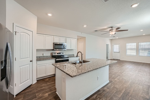 kitchen with light stone counters, stainless steel appliances, a kitchen island with sink, and white cabinets