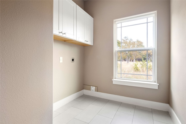 laundry room with hookup for an electric dryer, light tile patterned floors, a healthy amount of sunlight, and cabinets