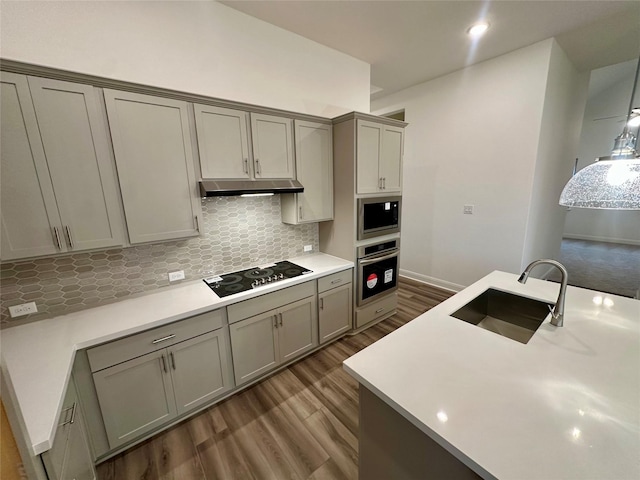 kitchen with sink, dark wood-type flooring, gray cabinetry, stainless steel appliances, and tasteful backsplash