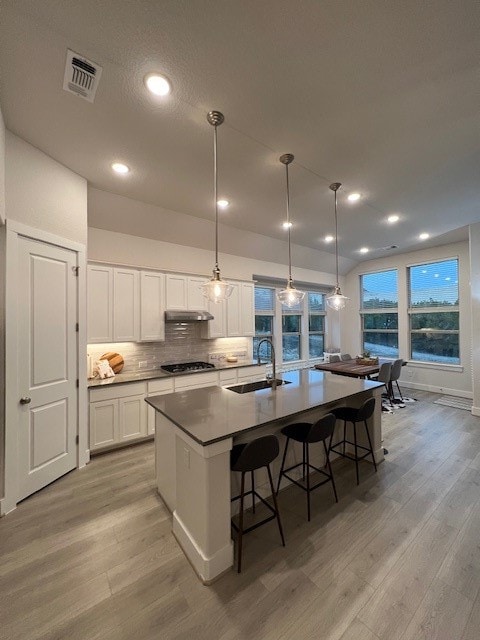 kitchen featuring sink, white cabinets, hanging light fixtures, and an island with sink