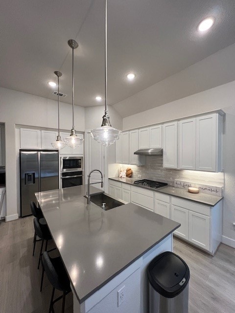 kitchen featuring appliances with stainless steel finishes, sink, light wood-type flooring, white cabinetry, and decorative light fixtures