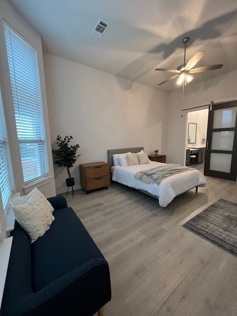 bedroom with ceiling fan, light hardwood / wood-style floors, and a barn door