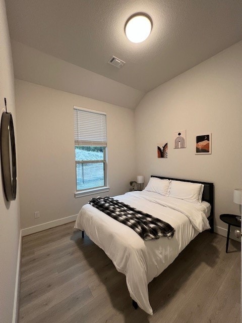 bedroom featuring a textured ceiling, vaulted ceiling, and dark hardwood / wood-style floors