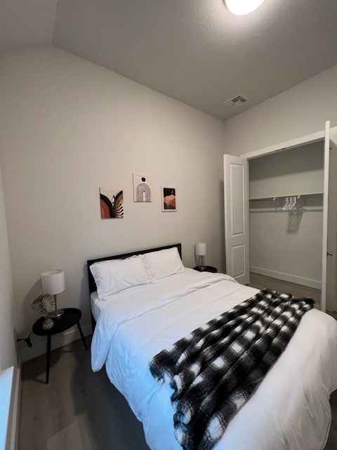 bedroom with a closet, hardwood / wood-style floors, a textured ceiling, and vaulted ceiling