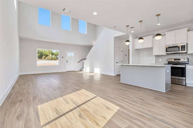 kitchen featuring appliances with stainless steel finishes, a kitchen island, hanging light fixtures, light hardwood / wood-style floors, and white cabinets