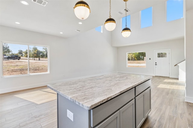 kitchen featuring hanging light fixtures, a kitchen island, light stone countertops, gray cabinetry, and light hardwood / wood-style floors