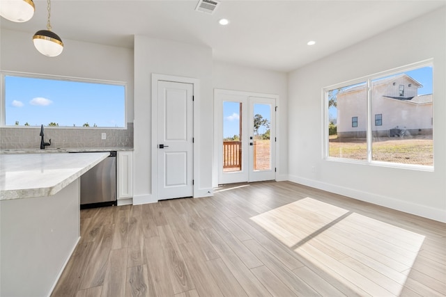 kitchen with backsplash, sink, pendant lighting, stainless steel dishwasher, and light hardwood / wood-style floors