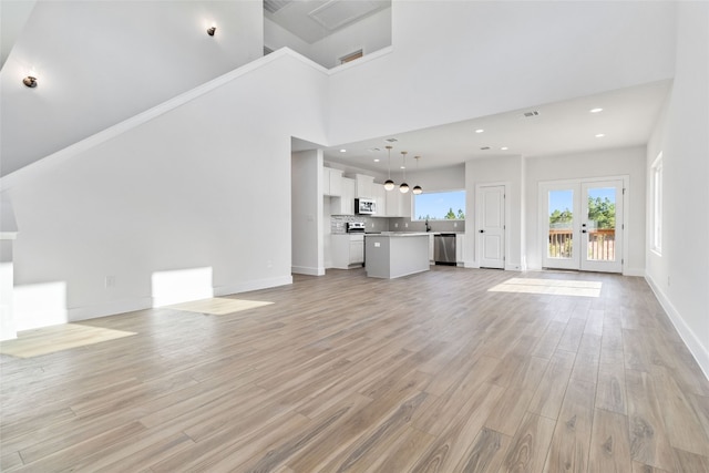 unfurnished living room featuring light hardwood / wood-style flooring, french doors, and a high ceiling