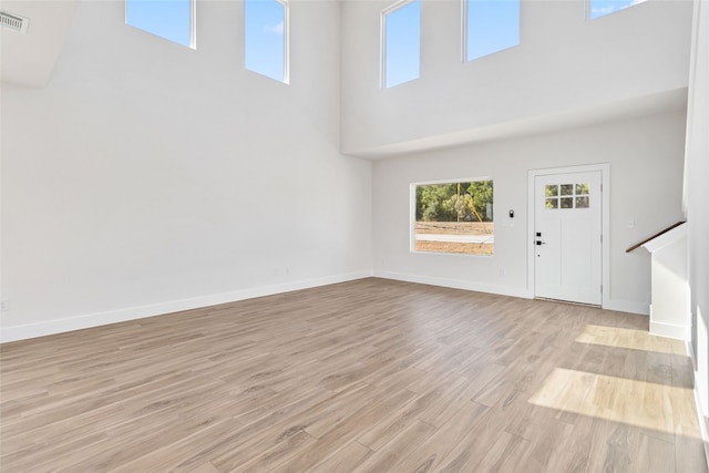 unfurnished living room with light hardwood / wood-style floors and a towering ceiling