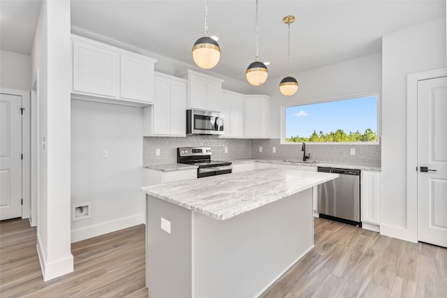 kitchen with appliances with stainless steel finishes, sink, a kitchen island, white cabinetry, and pendant lighting