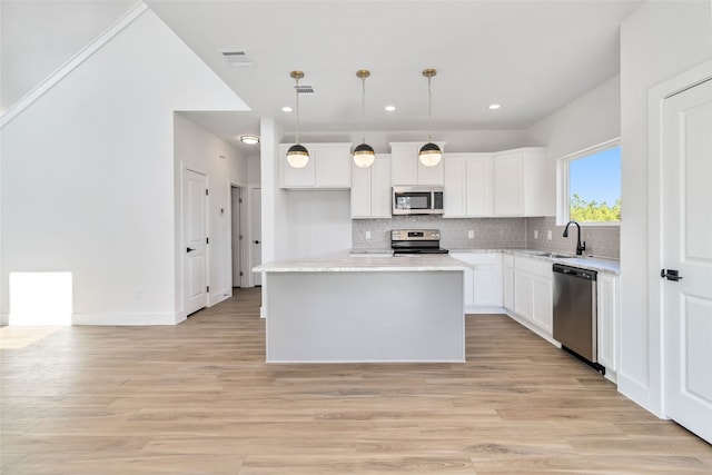 kitchen with a kitchen island, appliances with stainless steel finishes, pendant lighting, and light hardwood / wood-style floors