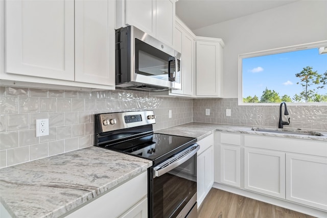 kitchen featuring decorative backsplash, appliances with stainless steel finishes, white cabinetry, light hardwood / wood-style flooring, and sink