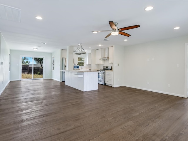 kitchen with wall chimney range hood, dark wood-type flooring, hanging light fixtures, stainless steel range with gas cooktop, and white cabinets