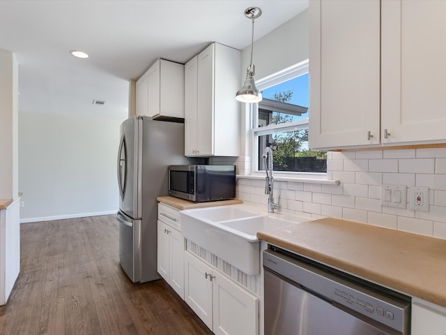 kitchen featuring white cabinetry, stainless steel appliances, decorative light fixtures, and dark hardwood / wood-style floors