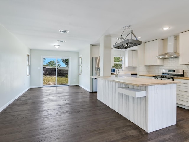 kitchen featuring white cabinets, dark hardwood / wood-style flooring, a kitchen island with sink, wall chimney exhaust hood, and stainless steel range with gas cooktop