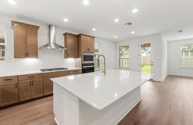 kitchen featuring wall chimney range hood, appliances with stainless steel finishes, visible vents, and light wood-style floors