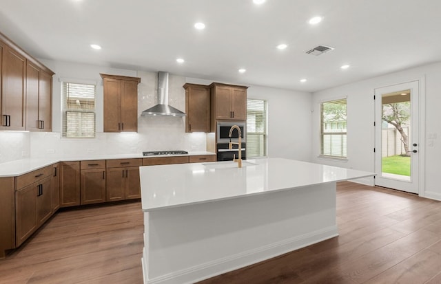 kitchen featuring a kitchen island with sink, visible vents, wood finished floors, gas stovetop, and wall chimney exhaust hood