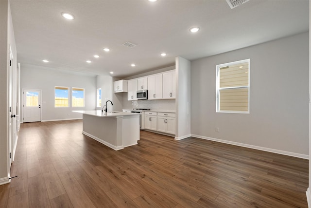 kitchen with stove, backsplash, a kitchen island with sink, sink, and white cabinetry