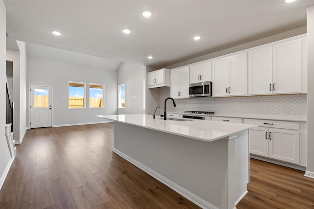 kitchen with decorative backsplash, dark wood-type flooring, sink, white cabinetry, and an island with sink