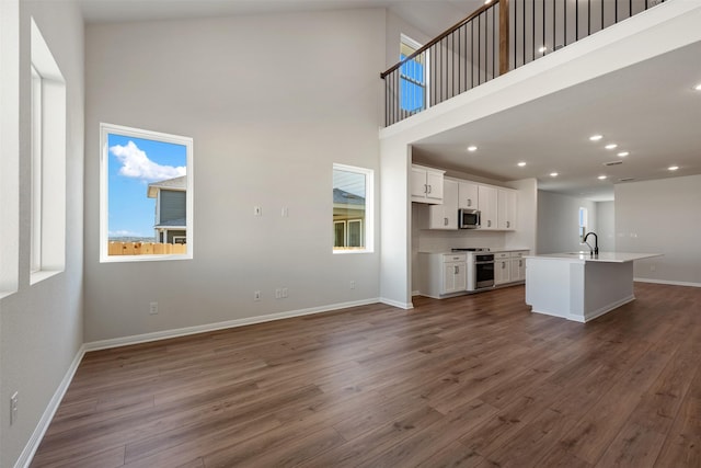 unfurnished living room featuring dark hardwood / wood-style flooring, sink, and a high ceiling