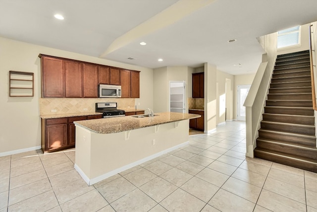 kitchen featuring light stone countertops, sink, stainless steel appliances, a breakfast bar, and a center island with sink