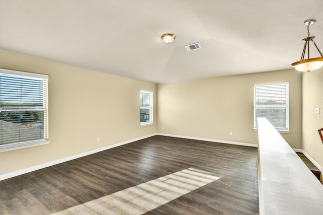 spare room with dark wood-type flooring, plenty of natural light, and vaulted ceiling