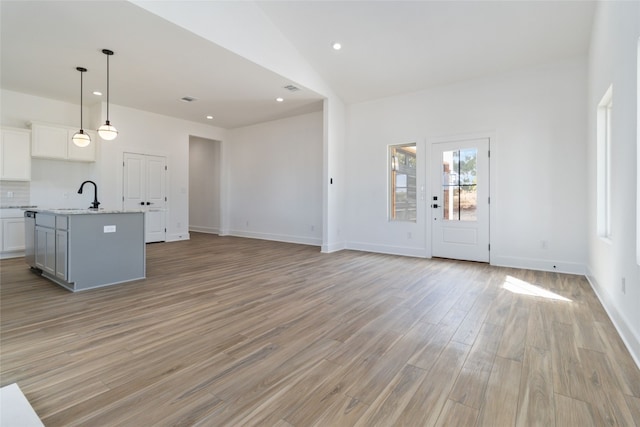 unfurnished living room featuring light hardwood / wood-style floors, lofted ceiling, and sink