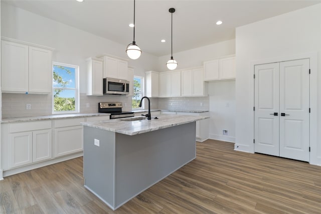 kitchen featuring appliances with stainless steel finishes, white cabinets, sink, and an island with sink