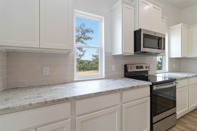 kitchen featuring light stone countertops, white cabinetry, appliances with stainless steel finishes, light hardwood / wood-style floors, and tasteful backsplash