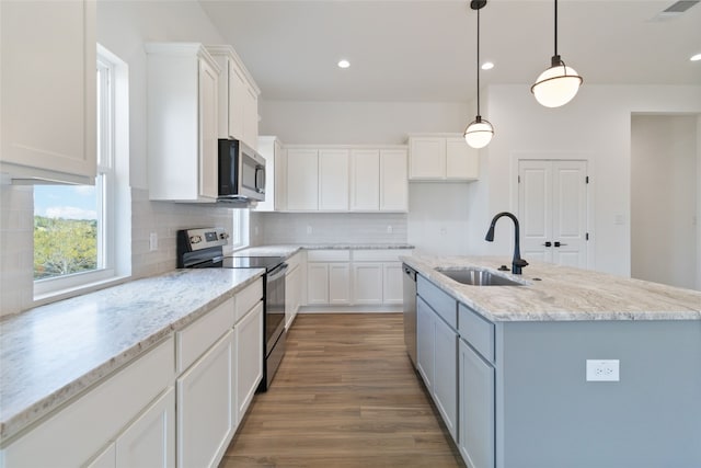 kitchen with appliances with stainless steel finishes, sink, white cabinetry, pendant lighting, and a kitchen island with sink