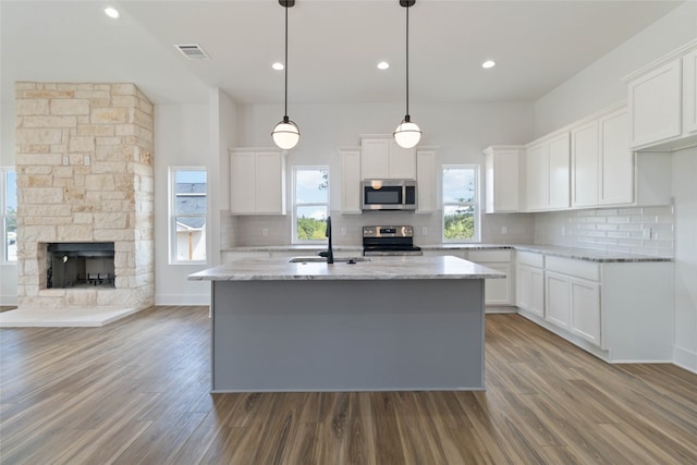 kitchen with appliances with stainless steel finishes, white cabinets, a kitchen island with sink, and wood-type flooring