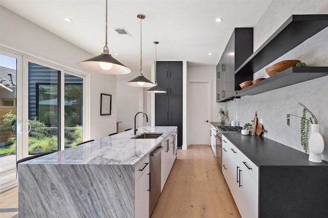 kitchen with white cabinetry, sink, light hardwood / wood-style flooring, dark stone counters, and decorative light fixtures