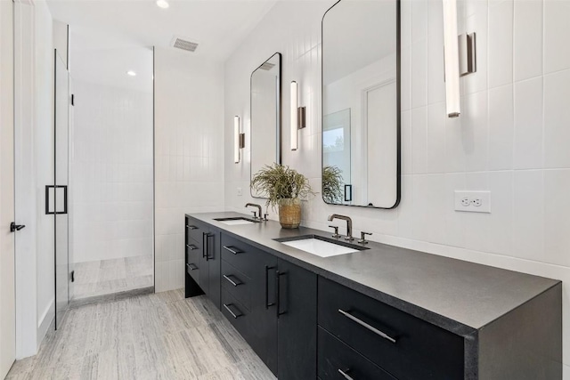 bathroom featuring hardwood / wood-style flooring, vanity, a shower with shower door, and tile walls