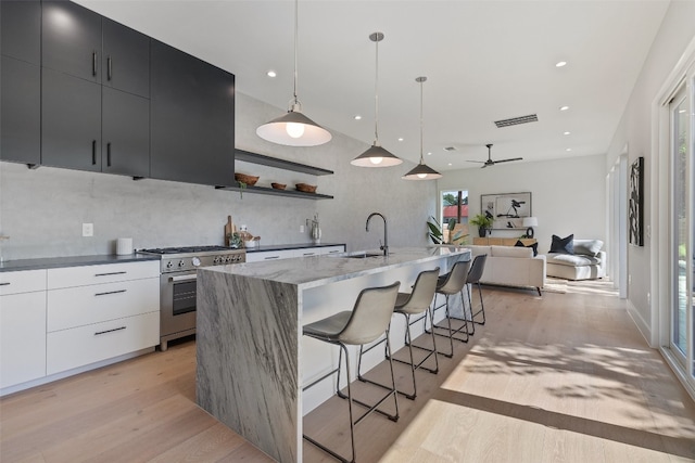 kitchen featuring light wood-type flooring, high end stainless steel range oven, ceiling fan, white cabinetry, and hanging light fixtures