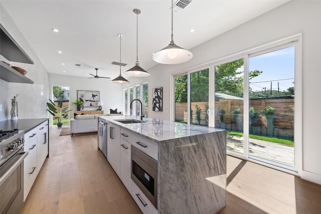 kitchen with a kitchen island with sink, white cabinets, sink, dark stone countertops, and stainless steel appliances