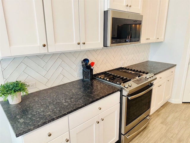 kitchen featuring backsplash, white cabinetry, stainless steel appliances, dark stone counters, and light hardwood / wood-style flooring