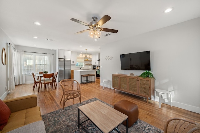 living room featuring ceiling fan, sink, and light hardwood / wood-style flooring