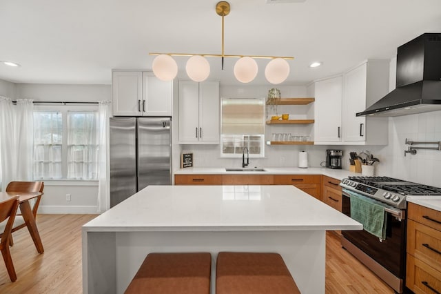 kitchen featuring sink, stainless steel appliances, wall chimney range hood, pendant lighting, and white cabinets