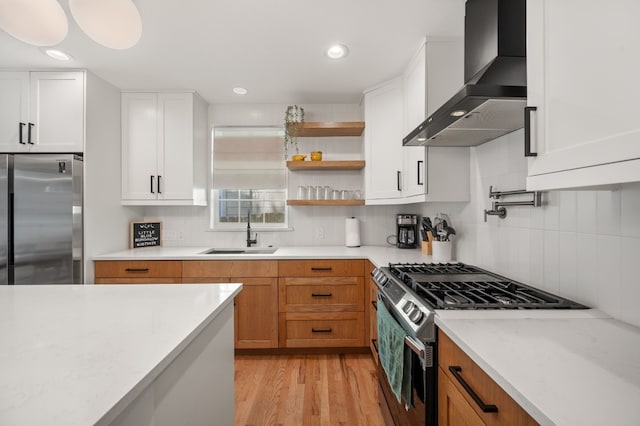 kitchen featuring backsplash, white cabinets, wall chimney range hood, sink, and appliances with stainless steel finishes