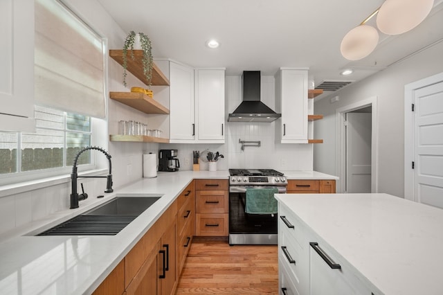 kitchen featuring white cabinetry, sink, stainless steel range with gas stovetop, and wall chimney range hood