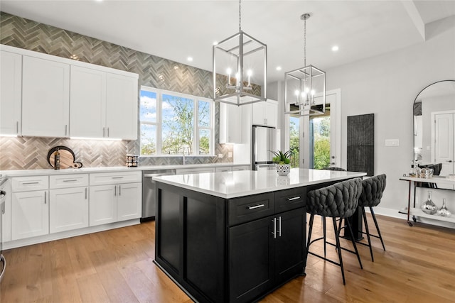 kitchen featuring appliances with stainless steel finishes, a center island, sink, white cabinetry, and decorative light fixtures