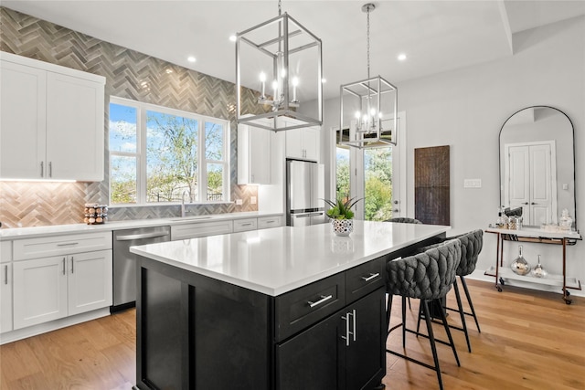 kitchen featuring hanging light fixtures, decorative backsplash, a kitchen island, white cabinets, and appliances with stainless steel finishes